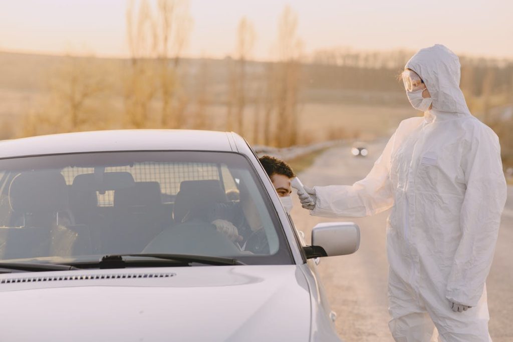 A person in a covid hazmat suit standing next to a car