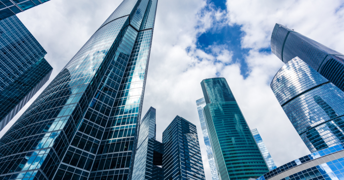Modern glass skyscrapers under a partly cloudy sky, viewed from a low angle looking upward.