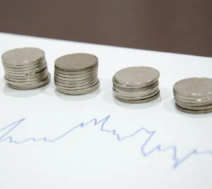 Stacks of coins arranged in increasing height on a sheet of paper with a blue financial line graph.