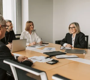 Business team gathered around a conference table with laptops and printed reports, discussing performance charts in a modern office setting.